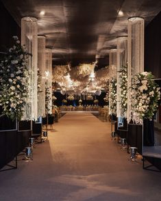 an aisle decorated with white flowers and chandelier hanging from the ceiling at night