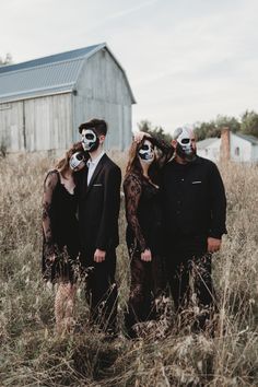 three people with painted faces standing in tall grass next to a barn wearing masks on their faces