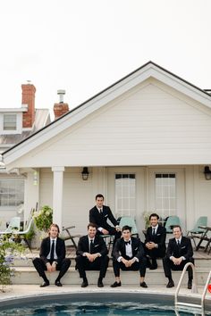 a group of men in suits sitting on the edge of a swimming pool next to a house