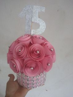 a hand holding a cupcake decorated with pink flowers and silver glitters on top