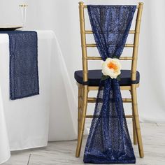 a blue chair with a flower on it next to a white table cloth and gold chairs