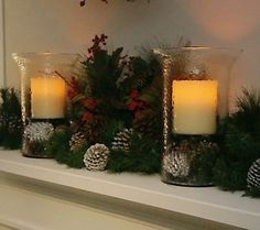 three lit candles sitting on top of a mantle covered in pine cones and greenery