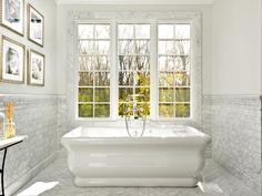 a large white bath tub sitting in a bathroom next to two windows with pictures on the wall