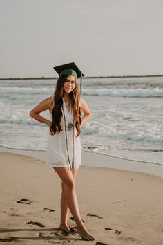 a woman in a graduation cap and gown standing on the beach with her hands on her hips