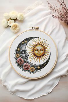 a cross - stitch sun and moon with roses on the table next to some flowers