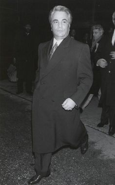 an old black and white photo of a man in a suit walking down the street