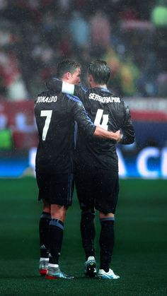 two soccer players in black uniforms standing on the field with their arms around each other