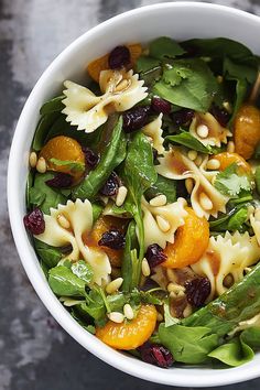 a white bowl filled with pasta, spinach and oranges on top of a table