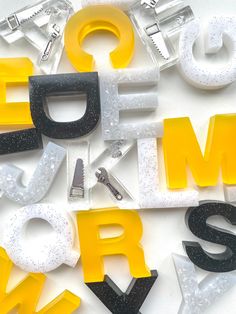 the letters are made up of different types of plastic and glittery shapes, with scissors in each letter