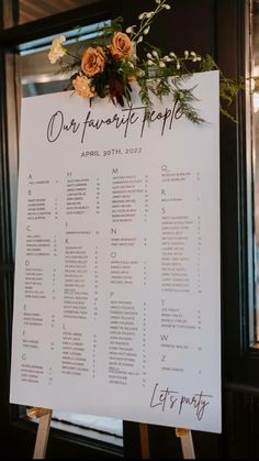 a sign that has flowers on top of it with the names of each wedding guests