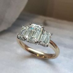 a three stone diamond ring sitting on top of a white cloth covered tablecloth with a pillow in the background