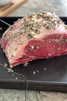 a piece of raw meat with herbs on it sitting on a black tray next to a knife