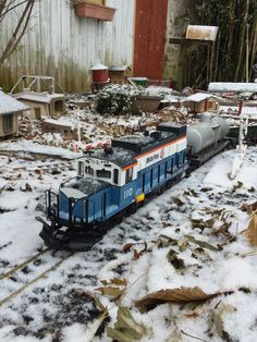 a blue and white train traveling through a snow covered yard next to a wooden building