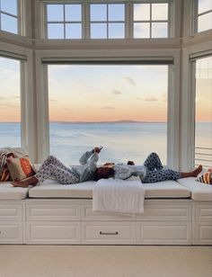 two people are lounging on a window sill in front of an ocean view