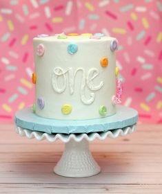 a white cake with colorful sprinkles and the word one on it