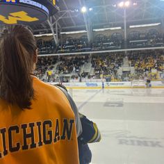 a woman in an orange hockey jersey is looking at the ice