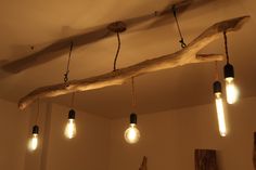 several light bulbs are hanging from a branch in a room with white walls and wood beams