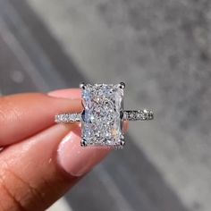 a person holding a ring with a cushion cut diamond in it's middle finger