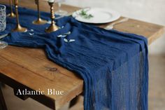 a wooden table topped with plates and glasses next to a blue cloth draped over it