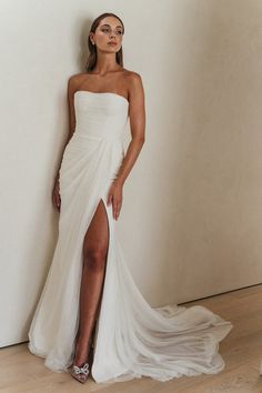 a woman in a white dress leaning against a wall with her leg up on the floor