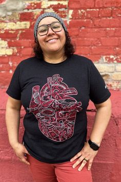 a woman standing in front of a brick wall wearing a black shirt with a red heart on it