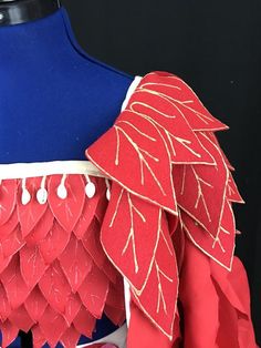 a dress made out of paper with red and white feathers on the shoulders, in front of a mannequin's head