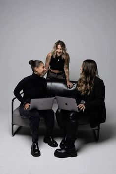 three women sitting on a couch with an open laptop in front of them, all looking at each other