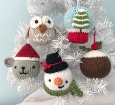 four knitted ornaments hanging from a white christmas tree with snowman, penguin and bear