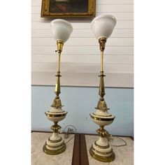 two lamps sitting next to each other in front of a wall with a painting on it