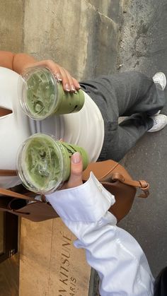 a person holding two cups with green liquid in them, while sitting on a chair