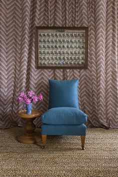 a blue chair sitting next to a table with flowers on it in front of a curtain