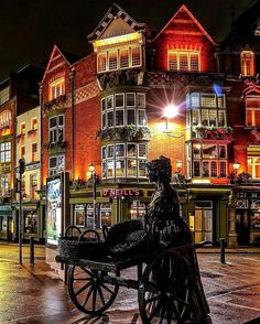 a statue sitting on top of a wooden bench in the middle of a city at night