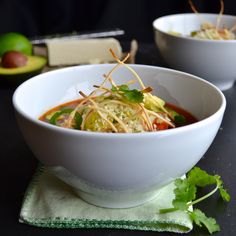 two white bowls filled with food and garnished with cilantro sprouts