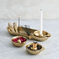 three gold bowls with candles and sticks in them on a white table top next to a candle holder