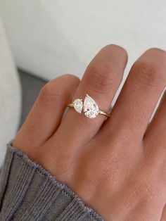 a woman's hand wearing a gold ring with two pear shaped diamonds on it