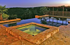 an outdoor swimming pool surrounded by stone steps and trees at dusk with the sun setting in the background