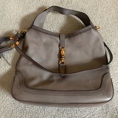 A Gucci Calfskin Duilio Brogue Large New Jackie Hobo Bag. This Gray Leather Bag Has A Removable Flat Leather Strap With Gold Tone Clasps And Anchors, A Flat Leather Adjustable Strap With Brogue Trim, Open Top With Gold Tone And Bamboo Style Piston Lock, Tassel Accent To One Side And Brogue Trim To The Top Lines And Along Base. The Interior Is Lined In Taupe Canvas With A Sidewall Zipper And Multiple Slip Pockets. Size: 16.5" W X 14.25" H X 2.5" D. Dust Bag Included. Excellent Condition! Gucci Hobo Bag, Black Dress Shoe, Tie Up Sandals, Gucci Monogram, Versace Collection, Gucci Bamboo, Hobo Style, Gucci Leather, Gray Leather