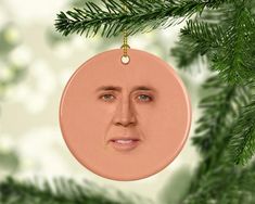 a christmas ornament with a face on it hanging from a pine tree branch