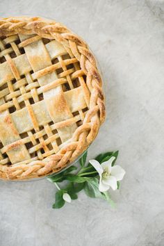 an overhead view of a pie on a table with flowers in the foreground and a single white flower next to it