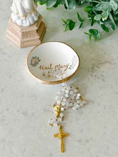 a rosary with a gold cross on it next to a small statue and green leaves