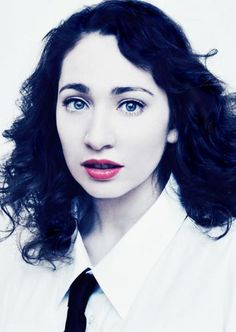 a woman with curly hair wearing a white shirt and black neck tie looking at the camera