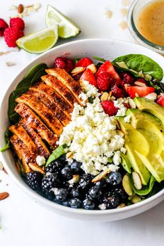 a bowl filled with fruit, avocado, strawberries, and chicken on top of a white table