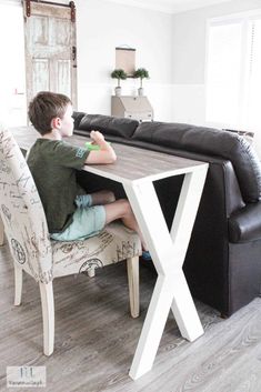 a young boy sitting at a table in front of a black couch with white x legs