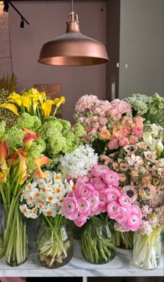 several vases filled with different types of flowers sitting on a table next to a lamp