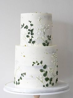 a three tiered cake with white flowers and green leaves