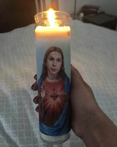 a hand holding a lit candle with the image of jesus on it