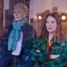 two women standing in front of a window with their arms crossed and looking at the camera