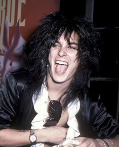 an image of a man with long black hair and piercings on his head laughing