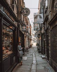 a woman is standing in an alleyway looking at her cell phone while she's walking down the street