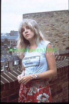 a woman standing on top of a building next to a brick wall and looking off into the distance